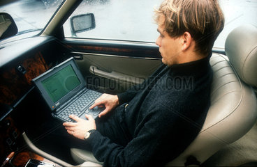 Mann sitzt im Auto und arbeitet am Laptop