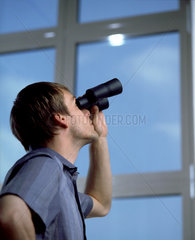 Ein Mann schaut mit dem Fernglas aus dem Fenster