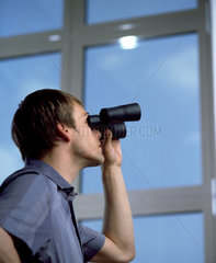 Ein Mann schaut mit dem Fernglas aus dem Fenster