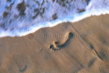 Fussspur im Sand wird von Welle umspuelt
