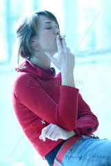 Junge Frau sitzt rauchend am Fenster