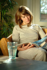 Junge Frau sitzt zu Hause in einem Korbsessel und liest eine Zeitschrift