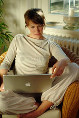 Junge Frau sitzt zu Hause in einem Korbsessel und surft im Internet