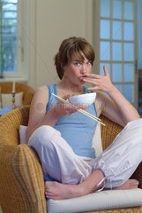 Junge Frau isst zu Hause mit Staebchen ein asiatisches Reisgericht aus einer Schale