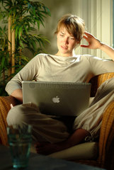 Junge Frau sitzt zu Hause in einem Korbsessel und surft im Internet