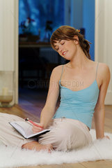 Junge Frau sitzt schreibend zu Hause auf einem Flokati