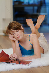 Junge Frau liegt zuhause auf einem Flokati und liesst in einer Zeitschrift