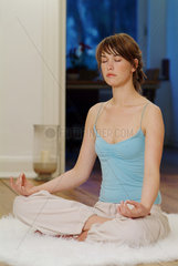 Junge Frau sitzt zu Hause und macht Yoga
