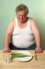 Dicker Mann in Unterhemd sitzt vor einem Teller mit Lauch