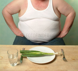 Dicker Mann in Unterhemd sitzt vor einem Teller mit Lauch