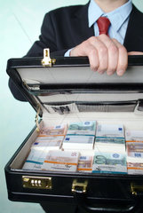 Ein Mann macht einen mit Euro-Buendeln gefuellten Koffer auf
