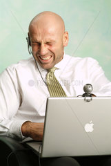 Mann arbeitet an seinem Powerbook und schaut zerknirscht in die Webcam