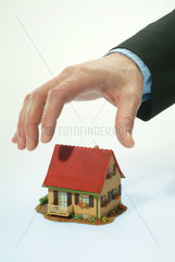 Eine Hand greift nach einem Einfamilienhaus-Modell