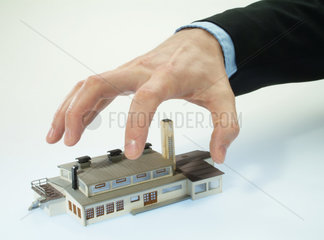 Eine Hand greift nach einem Fabrikmodell