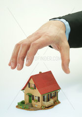 Eine Hand greift nach einem Einfamilienhaus-Modell