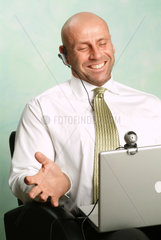 Mann arbeitet an seinem Powerbook und lacht in die Webcam
