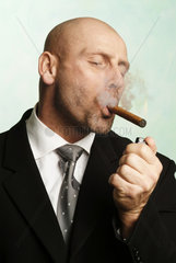 Mann zuendet sich genuesslich eine Zigarre an