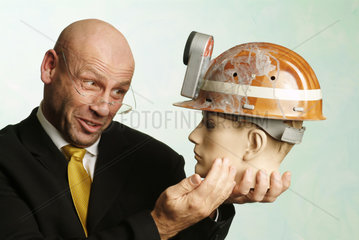 Mann haelt Puppenkopf mit Bergarbeiterhelm