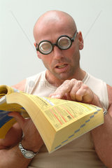 Mann mit dicker Brille versucht die Gelben Seiten zu lesen