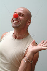 Muskuloeser Mann mit Clownsnase zieht eine Grimasse