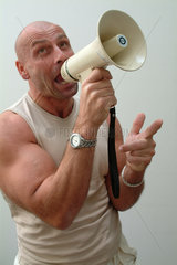 Muskuloeser Mann mit Glatze schreit in ein Megaphon