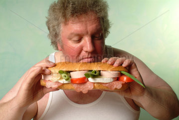Dicker Mann in Unterhemd isst ein riesiges belegtes Baguette