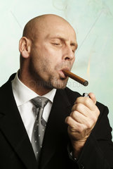 Mann zuendet sich genuesslich eine Zigarre an