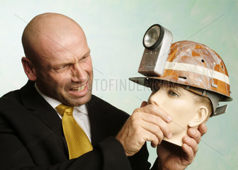 Mann haelt Puppenkopf mit Bergarbeiterhelm