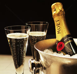 2 Champagnerglaeser stehen neben einem Kuehler mit einer Flasche MOET