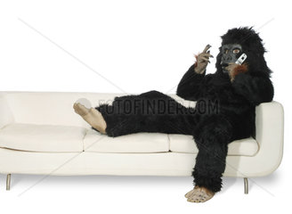 Mann in Gorillakostuem sitzt auf einer Couch und telefoniert