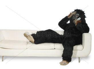 Mann in Gorillakostuem sitzt auf einer Couch und telefoniert