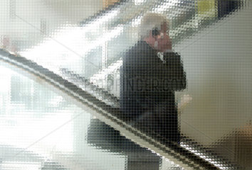 Manager mit Handy faehrt die Rolltreppe abwaerts