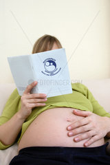 Schwangere  junge Frau liest im Mutterpass