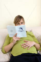 Schwangere  junge Frau liest im Mutterpass