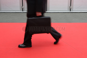 Ein Geschaeftsmann mit Koffer geht ueber einen roten Teppich