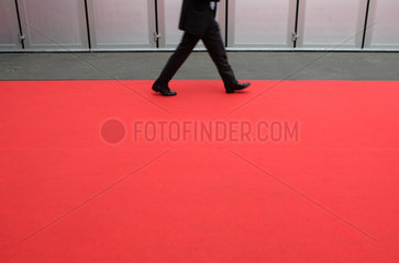 Ein Geschaeftsmann geht ueber einen roten Teppich