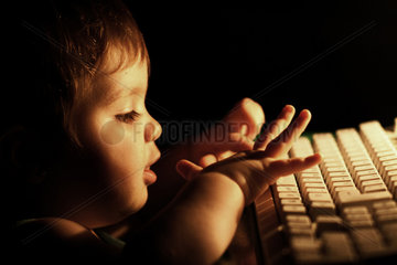 Spanien  kleines Maedchen tippt abends auf einer PC-Tastatur
