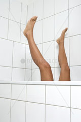 Junge Frau streckt ihre Beine aus der Badewanne