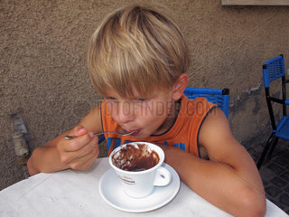 Berlin  Deutschland  Junge leckt gedankenverloren seinen Loeffel mit Kakao ab