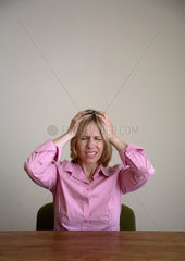 Frau sitzt mit Kopfschmerzen am Tisch