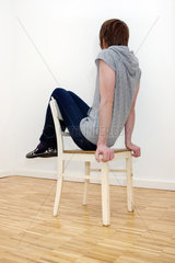 Berlin  Deutschland  schlanker junger Mann in Roehrenjeans sitzt auf einem Stuhl