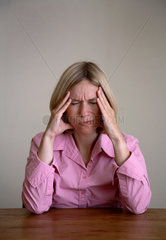 Frau sitzt mit Kopfschmerzen am Tisch