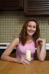 Junge Frau sitzt in ihrer Kueche am Tisch bei einem Glas Milch