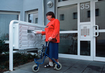 Wohnen im Alter  gehbehinderte Frau am Briefkasten