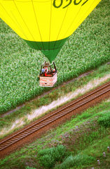 Heissluftballon fliegt ueber Bahnstrecke und Maisfeld