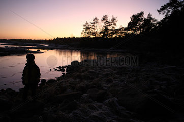Vaestervik  Schweden  Silhouette  Kind steht in der Daemmerung allein an einem See
