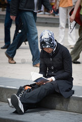 Berlin  Deutschland  junge Frau mit Kopftuch sitzt lesend auf einer Treppenstufe