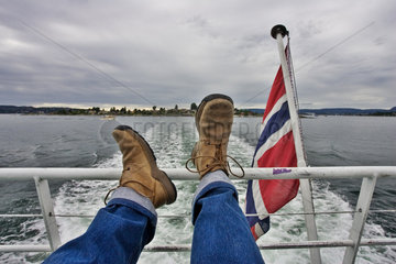 Maennerbeine auf einer Schiffsreling hochgelegt  neben einer norwegischen Flagge