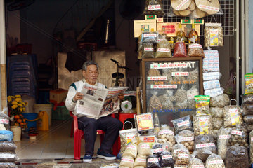 Ein Haendler sitzt vor seinem Geschaeft in der Altstadt von Hanoi