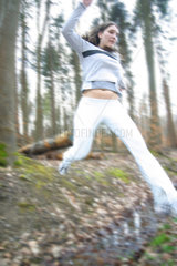Frau springt beim Waldlauf ueber einen Graben